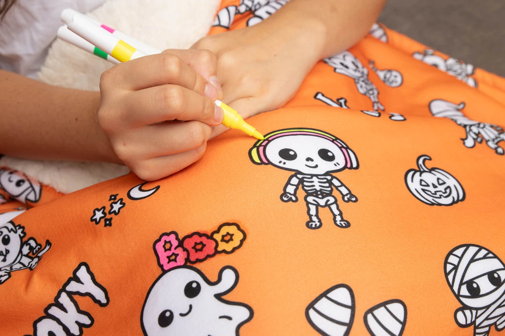 Hands adding bright color to the Halloween blanket with fabric markers